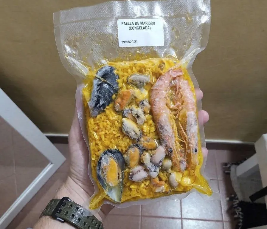 Bolsa de paella de marisco congelada y envasada al vacío, con gambones y mejillones, sostenida en la mano